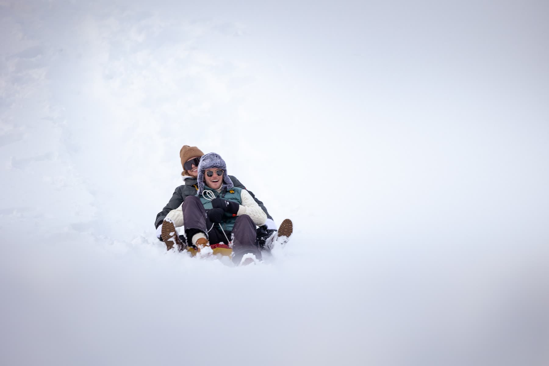Two friends sledding down a snowy slope at Fýri